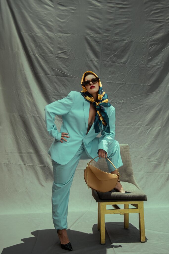 Stylish woman in a pastel suit posing with a chair and handbag indoors.